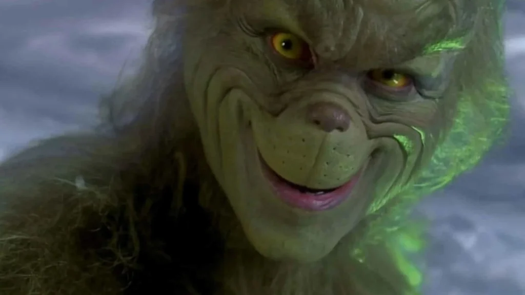 The Grinch from How the Grinch Stole Christmas giving a mischievous, close-up grin with glowing yellow eyes.