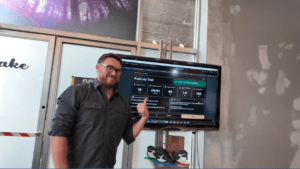 Jeff Turner smiling and pointing at a push-up test readout screen inside Fuse Maker Space while testing custom fitness technology.