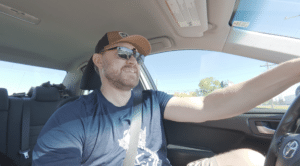 Jeff Turner wearing sunglasses and a brown cap driving his car on a day trip road trip.